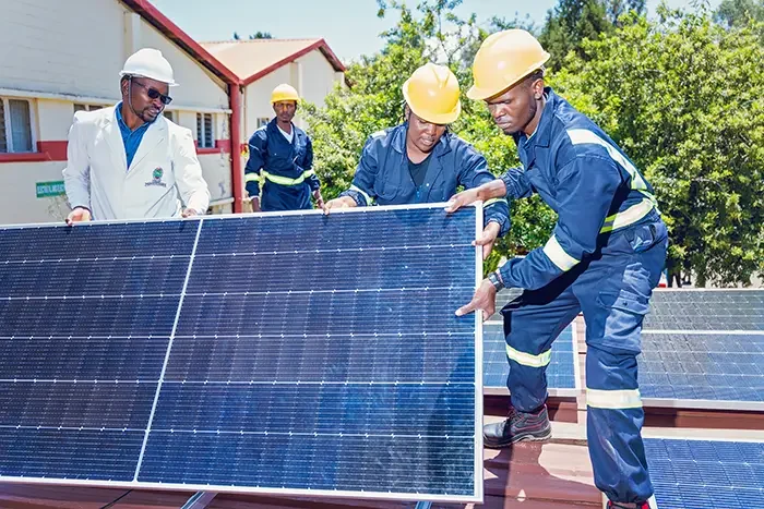 Instructor guiding trainees while lifting a solar panel at a WTS Foundation training site in Kenya